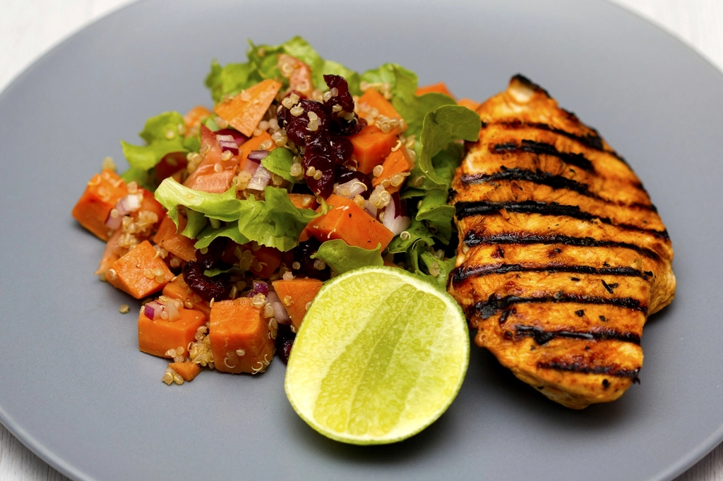 A balanced plate of grilled chicken with a quinoa, sweet potato and green salad